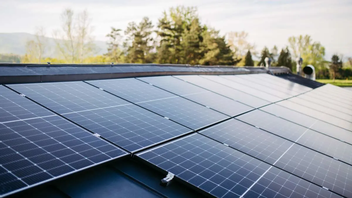 Paneles solares instalados sobre el techo de una casa, con árboles y montañas al fondo